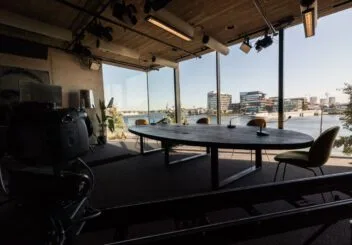 Das Crowdale-Studio, mit einem Tisch und vier Sitzplätzen. Durch die großen Fenster ist der Fluss &#039;t IJ sichtbar.